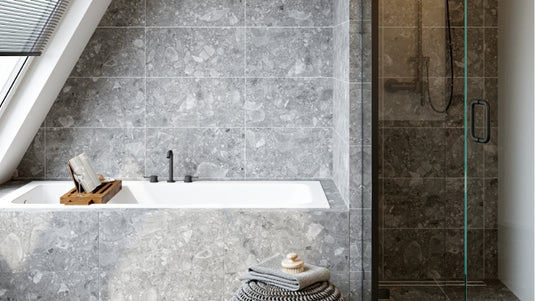 Modernes Badezimmer mit grauen Natursteinfliesen, eingebauter Badewanne und Glasduschkabine.