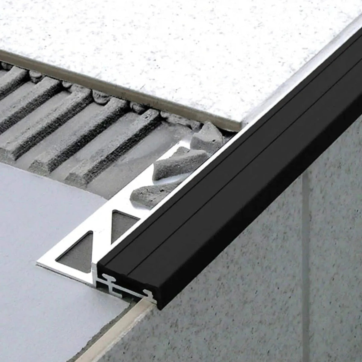 Profilé d'escalier encastré sous le carrelage avec un insert étroit en caoutchouc noir. Une partie du côté estampé est libre dans le lit de colle. #FR0001744
#FR0001748