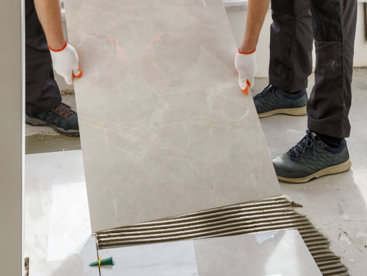 Handwerker verlegt eine große Marmorfliese auf frischen Fliesenkleber mit präziser Ausrichtung.