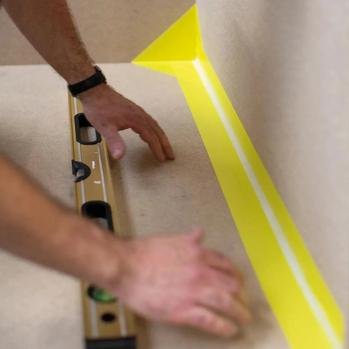 Eine Person richtet das gelbe Dichtband selbstklebend WS im Übergang zwischen Boden und Wand aus