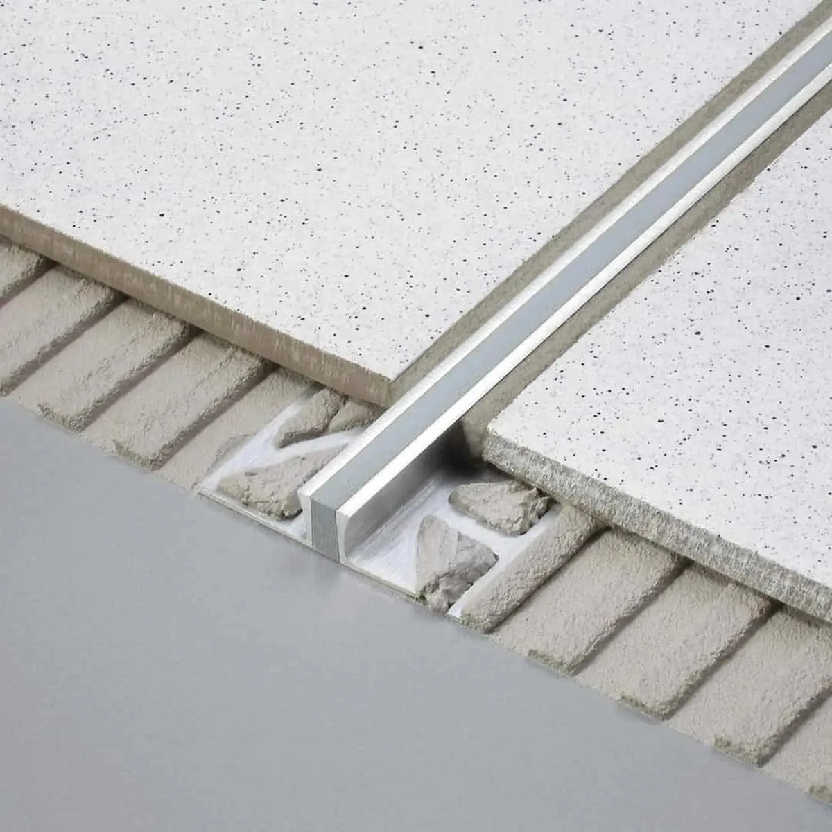 Unter weißen Fliesen verbautes DURAL Dehnungsfugenprofil aus Edelstahl. Ein Teil des Profils liegt frei im Kleberbett