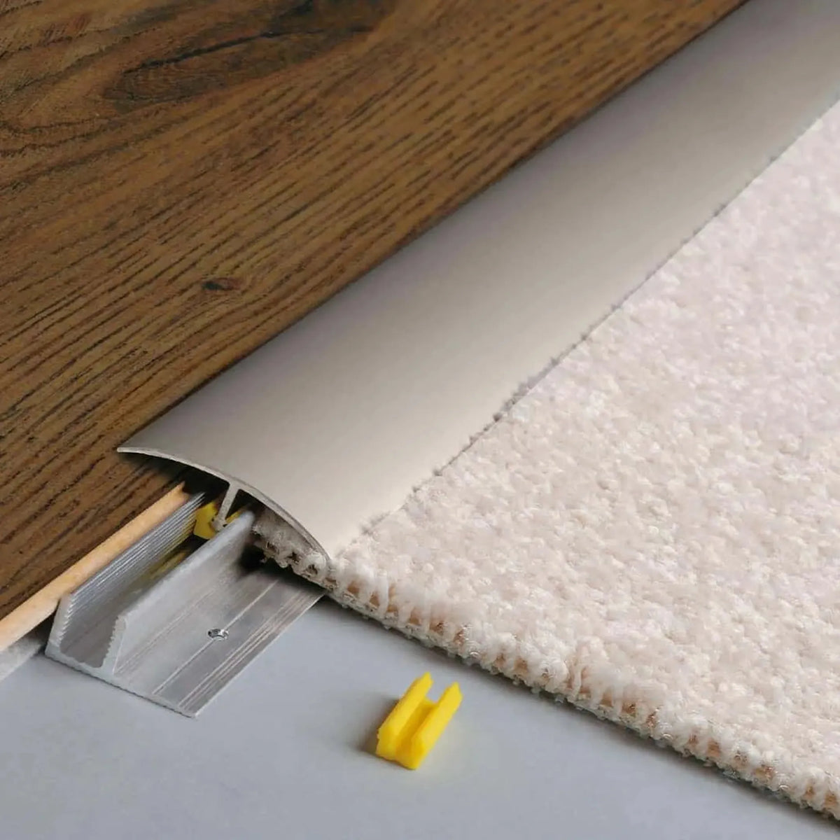 Installed titanium anodised height adjustment profile CLIP. Brown inserted wood floor on one side and light carpet floor on the other side #A0003687 #A0003688