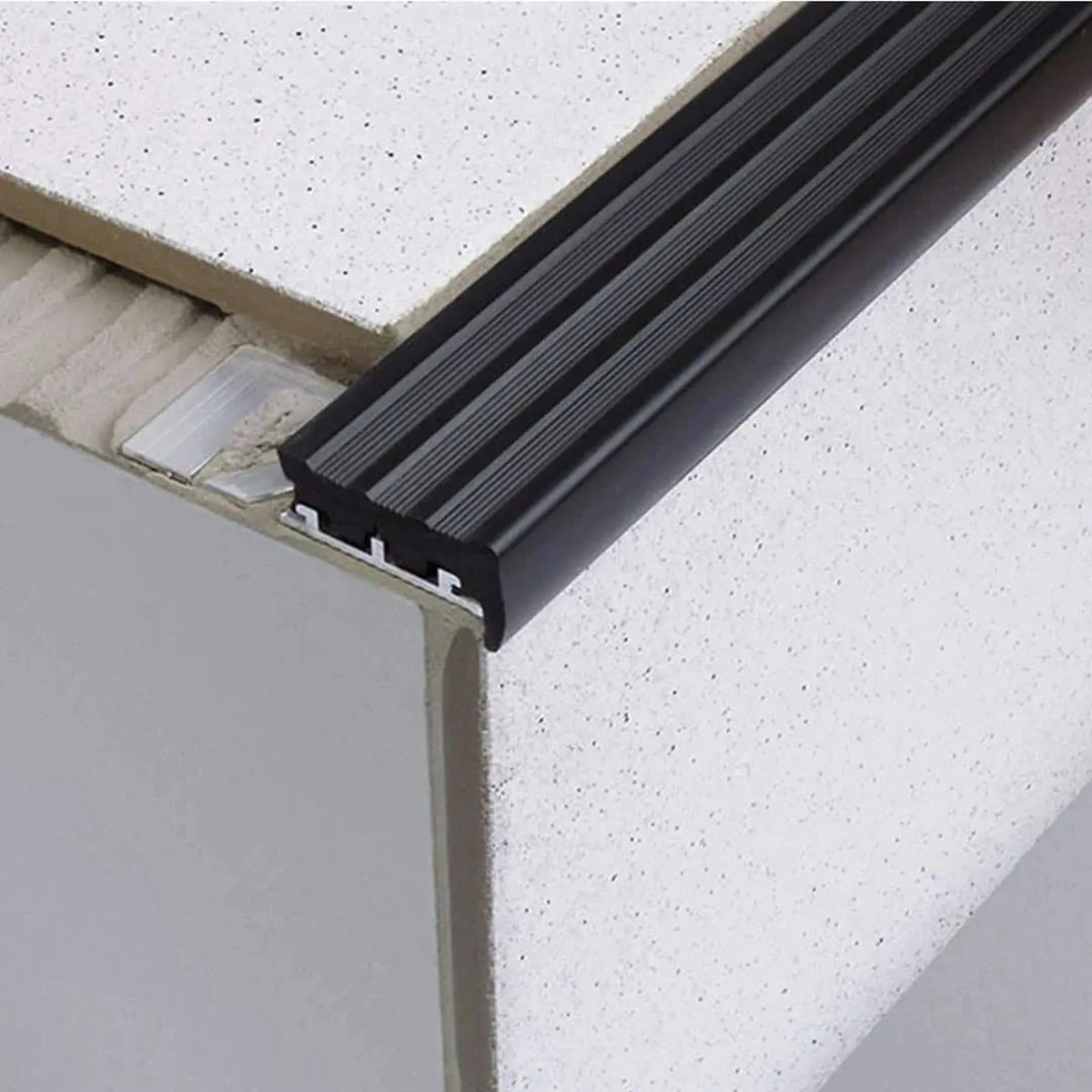 Stair profile with wide rubber insert in black installed under tile. Part of the punched leg is exposed in the adhesive bed #A0001752 #A0001756