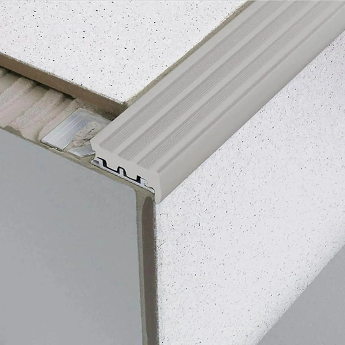 Stair profile with wide rubber insert in grey installed under tile. Part of the punched leg is exposed in the adhesive bed #A0001753 #A0001757