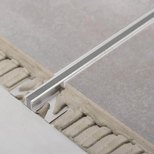 Unter grauen Fliesen verbautes DURAL Dehnungsfugenprofil aus Aluminium. Ein Teil des Profils liegt frei im Kleberbett