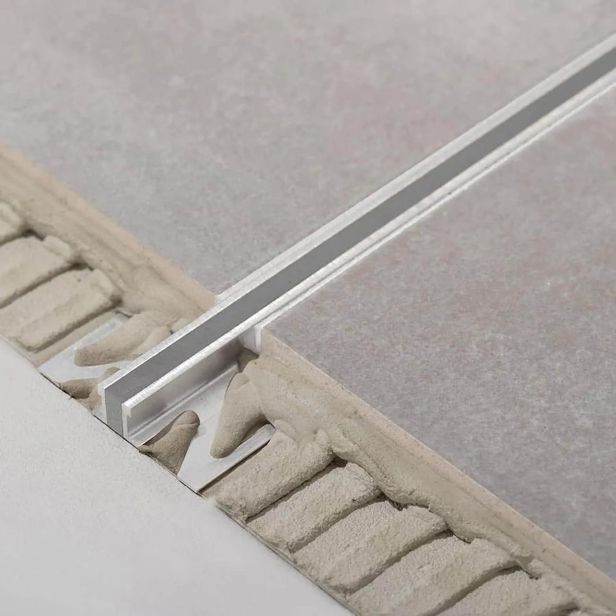 Unter grauen Fliesen verbautes DURAL Dehnungsfugenprofil aus Aluminium. Ein Teil des Profils liegt frei im Kleberbett